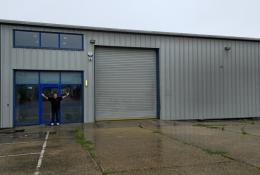 A bald man dressed in black outside a non-descript industrial estate