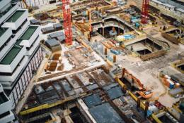 A costruction site with several peices of equipment including a red tower crane and a yellow excavator