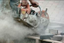 A close up of a hand-held concrete saw in use with silica dust clouds