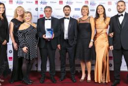 A group of people in evening wear in a line, on a stage accepting an award