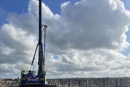 A Junttan piling rig stands in front of hundreds of pile caps, with a blue sky and dramatic clouds