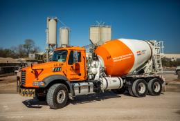 A bright orange concrete mixer truck at a cement plant