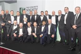 Lots of men in a line wearing black tie celebrate winning the Concrete Society’s annual Awards for Excellence in Concrete 2024 at The Royal Lancaster London