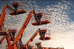 Orange aerial work platforms set against a backdrop of white, fluffy clouds