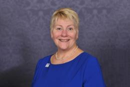 A head and shoulders photo of Caroline Gumble, CEO, Chartered Institute of Building (CIOB), wearing a blue dress, brooch and necklace.