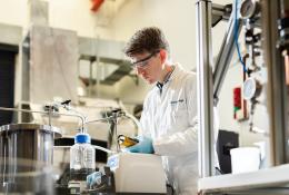 A man in lab coat and safety goggles working in a laboratory.