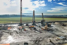 A large open area of country side with a crane and two piling rigs during construction of a circular tank that will be used to store radioactive waste in Slovenia.