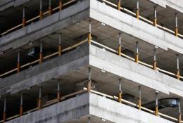 This image depicts a close-up view of a concrete multi-story building under construction, highlighting the raw structural elements such as concrete slabs and metal supports. The image conveys a sense of industrial progress and urban development in a modern city.