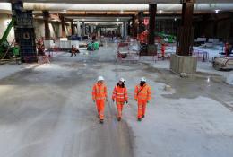 Three people in orange PPE walk across the competed base slab in the 850m long underground station box at Old Oak Common.