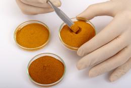 A close up of two hands holding one of three vials with a variety of orange powder
