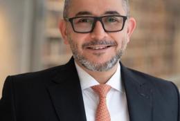 Mohamad Al-Dah, the new IStructE President 2025, in a dark suit, white shirt, glasses and an orange tie.
