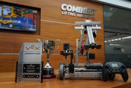 The Vex Robotics Awards on a table in front of a Combilift sign and video display showing a yellow and blue robotic vehicle