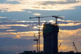 A High rise building under construction in silhouette with the sun setting behind it with three tower cranes