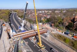 An aerial view of the new M67 St Annes Bridge under construction with a yellow crane on the near side of the bridge and a white crane on the far side.