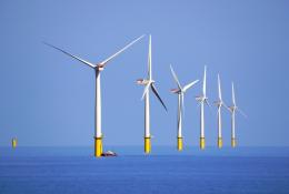 Six white and yellow wind turbines on a calm sea, part of the Walney Offshore Windfarm. Image: David Nixon / Creative Commons.