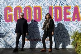 Ruth Sparkes and Sunita Gordon, co-founders of SaferSpace, dressed in black, photographed in harsh sunlight against a map of London with the slogan "Good Idea" printed over it.