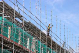 A construction worker in hard hat and PPE working on a scaffold.