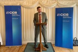 Mike Reader MP, the new chair of the All-Party Parliamentary Group for Excellence in the Built Environment, stands behind a podium, flanked by CIOB banners, speaking at the launch of the CIOB's Construction Client Guide: Leading Projects in the Built Environment, in Parliament last week.