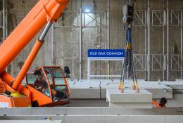An orange crane and orange PPE-clad worker installing the first platforms at HS2's Old Oak Common station for HS2 trains.