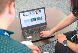 Two people look at a laptop screen which shows several photos and text related to sustainable construction