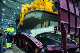A yellow and blue PPE clad worker in a factory uses a mould and lifting device for precast tunnel segments, France, CBE