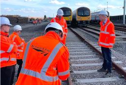 A group of people in Network Rail branded PPE inspect a concrete railway sleeper. The first-generation low-carbon concrete sleepers were installed by Concretene at GCRE in South Wales using 3.75 kg less cement per unit.