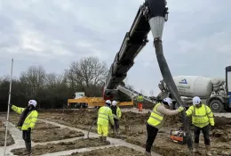 construction workers in yellow PPE lay concrete that's being delivered via chute from a concrete mixer