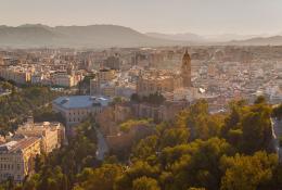 A panoramic photo of Malaga city centre with mountains in the distance, with the bullring lower right and a large church middle left.