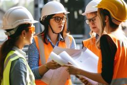 In the warm glow of the afternoon sun, a team of construction professionals gather closely, passionately engaged in a project discussion. Clad in safety helmets and high-visibility vests, they exchange ideas over blueprints, their collaboration a testament to the intricate planning that underpins successful infrastructure projects. Each individual's focused expression underscores the importance of each decision in the grand tapestry of urban development.