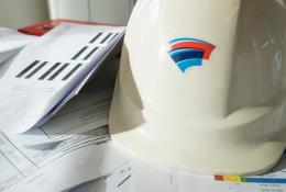 A white hard hat with red and blue insignia, and technical construction papers on a table