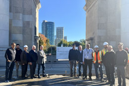 A group of people in business wear and PPE celebrate the use of Bio Graphene Solutions’ graphene-enhanced low-carbon concrete beneath Toronto’s historic Princes’ Gates at Exhibition Place.