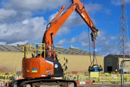 An orange, zero tail-swing midi excavator lifts a pile cropper on a construction site