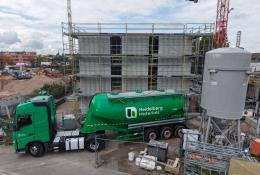A green, Heidelberg Materials' cement truck in front of an under construction house