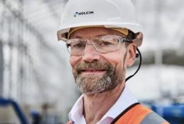 A head and shoulders photo of a man with a beard and glasses wearing PPE and a white hard hat