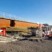 A steel bridge deck being slid into position with a crane in the background