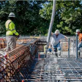 Four US construction workers in bright tshirts and PPE pour concrete
