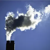 The top of a smoking industrial chimney with black and white smoke billowing from the top