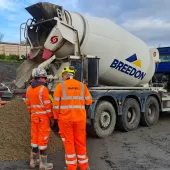 Two men in orange PPE in front of a concrete ready mix truck