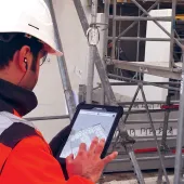 A man in orange PPE looking at a tablet screen