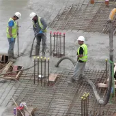 Three UK construction workers in PPE using a concrete pump to place concrete