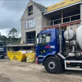 Two blue and grey concrete mixer trucks outside a new build house