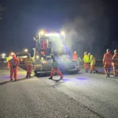 People in PPE repair a road at night