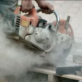 A close up of a hand-held concrete saw in use with silica dust clouds