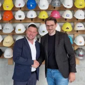 Christoph Miks (director customer solutions, core sensing), Michel Seeger (CEO, Vemaventuri) shake hands in front of a wall of multi-coloured construction hats