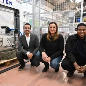 Three people crouch in front of the UK's first 3-D concrete printer