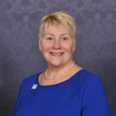 A head and shoulders photo of Caroline Gumble, CEO, Chartered Institute of Building (CIOB), wearing a blue dress, brooch and necklace.