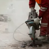 A man in red PPE using a hand-held concrete saw to repair a pavement
