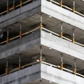 This image depicts a close-up view of a concrete multi-story building under construction, highlighting the raw structural elements such as concrete slabs and metal supports. The image conveys a sense of industrial progress and urban development in a modern city.