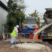 Workers at a construction site spread concrete being discharged by a mobile concrete mixer