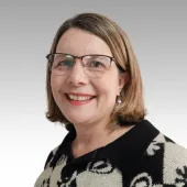 A head and shoulders photo of a woman in glasses, with shoulder length auburn hair, wearing a black and white top.